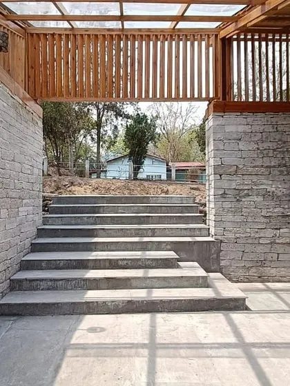 **Angling Centre, Pancheshwar:** The entrance to the centre is framed by local stone walls and a wooden screen, creating a transition from the outdoors into the main space. The steps are integrated into the landscape, following the natural terrain.