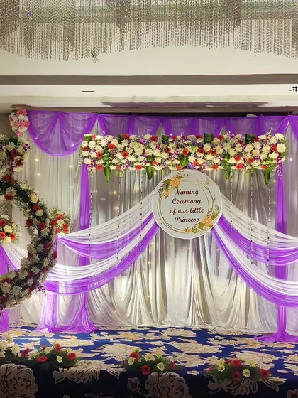 A lovely stage for a little princess's naming ceremony. I used lavender and white fabric drapes and floral arrangements to create a soft and elegant backdrop, featuring a large floral heart and a decorative nameplate.