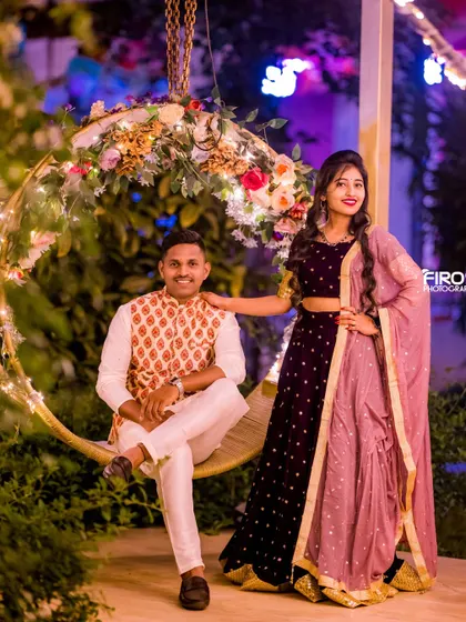 A happy couple poses on a decorated swing. The floral decorations and their stylish traditional outfits make for a very pretty and joyful portrait.