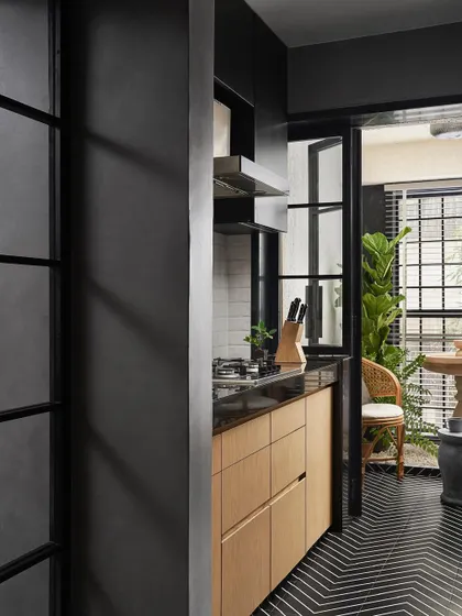 The parallel kitchen in Zen House features a chevron-patterned tile floor that flows from the kitchen into an adjacent fountain area. A gridded glass partition provides a view through to the serene outdoor space.