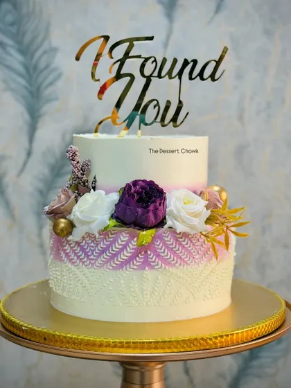 An elegant two-tier engagement cake with a unique stencil pattern on the bottom tier. The design is finished with beautiful flowers and a custom "I Found You" topper.