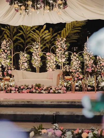 A perspective of the reception stage from a distance, framed by foreground flowers. This view shows the depth and dimension of the floral arrangement, making the stage feel like a secret garden.
