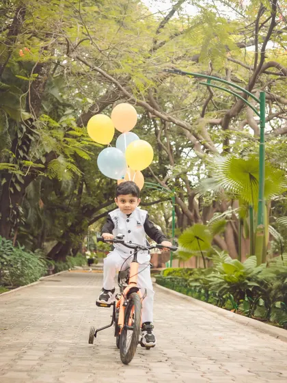 A happy boy riding his bike down a park path with balloons. Outdoor milestone shoots are perfect for capturing a child's favorite activities.