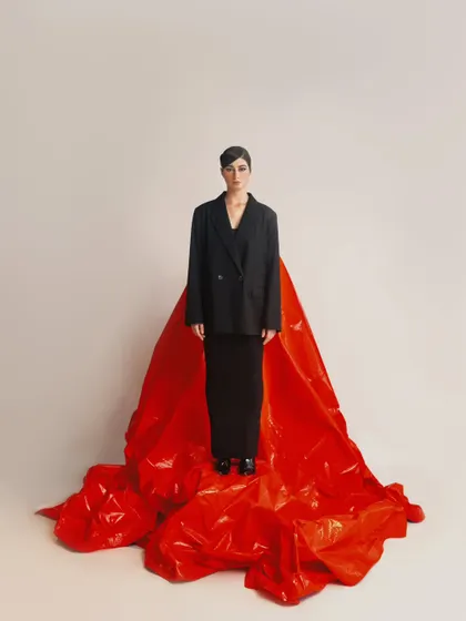 A minimalist, full-length fashion portrait. The composition is clean and powerful, emphasizing the model's silhouette.