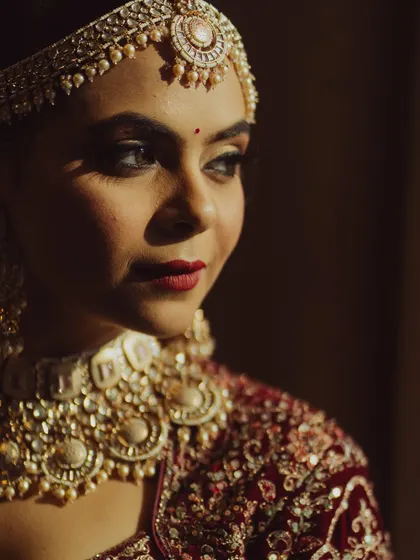 A close-up portrait with dramatic, moody lighting. The focus is on the bride's expressive eyes and the classic red lip, creating a look of timeless beauty.