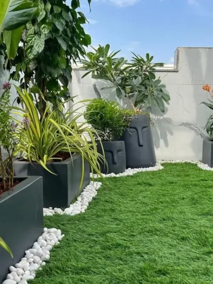 A closer look at the details of our terrace design. The combination of modern grey planters, unique face-themed pots, and a bed of white pebbles adds texture and personality to the vibrant green turf.
