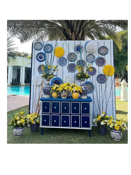 An elegant photo booth we designed for a Blue Pottery themed Haldi. The setup included a custom-painted chest of drawers, floral arrangements, and decorative plates.