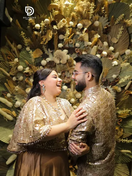 A candid moment of shared laughter between a couple during their Roka ceremony, highlighting their sparkling gold outfits and the genuine happiness of starting their journey together.