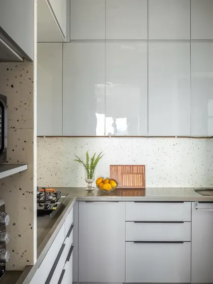 The kitchen is sleek and modern, with glossy white cabinets and a terrazzo backsplash and countertop. This design choice keeps the space bright and clean while adding a touch of playful pattern.