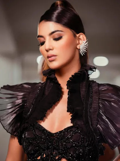 A softer, more introspective moment from the all-black editorial shoot, focusing on the delicate details of the ruffled collar and statement ear cuff.