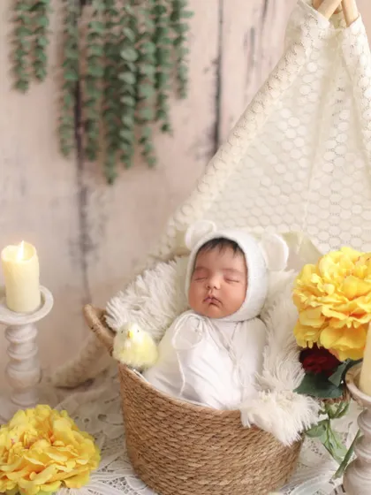 A peaceful scene with soft, warm lighting. This baby, wearing a cute bear bonnet, sleeps in a basket surrounded by candles and yellow flowers, creating a cozy and timeless feel.