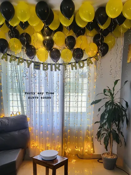 A simple home birthday setup with black and yellow helium balloons on the ceiling and a "Happy Birthday" banner.