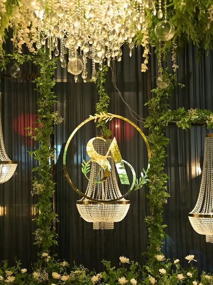 A close-up of a custom monogram and hanging crystal chandeliers, framed by greenery, designed as a key focal point within a larger floral installation.