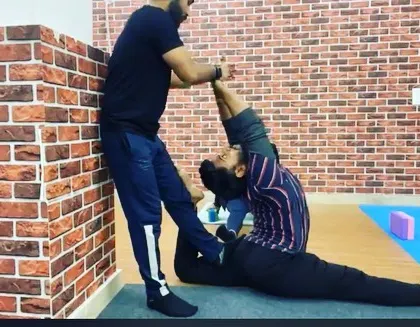 An instructor helps a student deepen their Eka Pada Rajakapotasana (One-Legged King Pigeon Pose), ensuring the backbend is safe and effective.