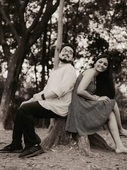 A playful shot of Anjum and Soham sitting back-to-back on a tree stump in the woods. This shows their fun side while still feeling natural and connected to the serene environment.