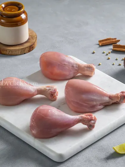 Four raw chicken drumsticks on a white marble board, a clean and minimalist shot for an e-commerce meat supplier.