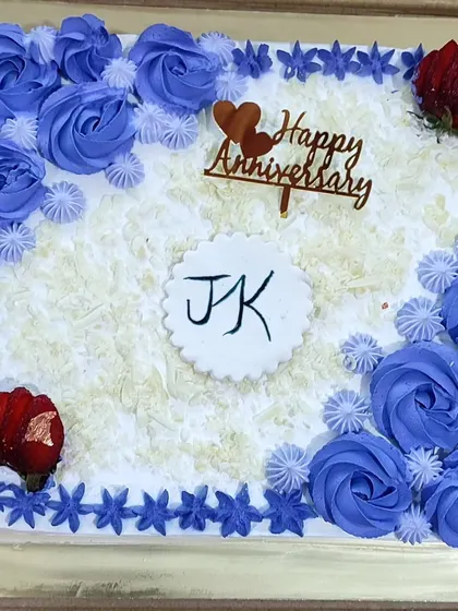 A square anniversary cake with white chocolate shavings and purple rose piping.