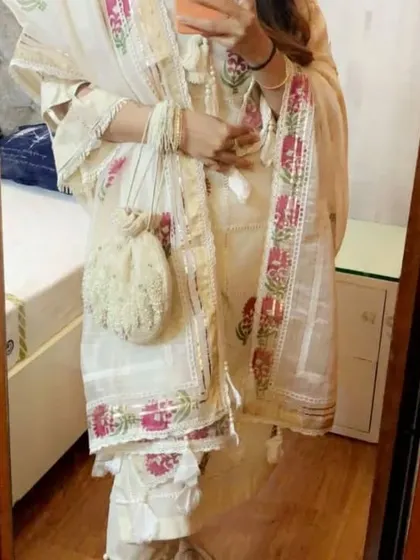 A client looking lovely in a custom off-white suit with pink floral block prints. The look is completed with a matching embroidered potli bag, showcasing how we can create coordinated accessories.