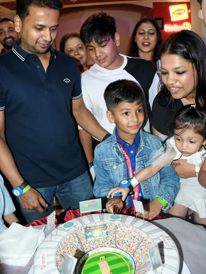 A wonderful family photo capturing the joy of the celebration around the highly detailed cricket stadium cake.