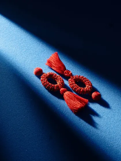 Red tassel earrings shot with dramatic, high-contrast lighting. The single sliver of light on the deep blue background creates a moody, mysterious, and very artistic image.