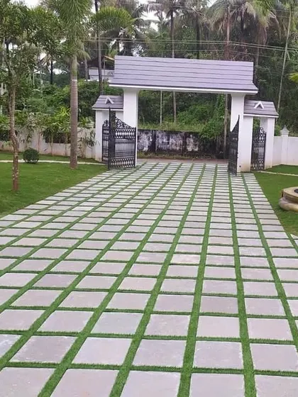 A wide shot of a driveway and entrance gate we designed for a large estate. The grid pattern of stone pavers and grass creates a visually impressive approach, surrounded by manicured lawns and palm trees.
