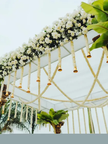 A close-up of the beautiful details on a traditional mandap, featuring hanging jasmine garlands and brass temple bells that chime with the breeze.