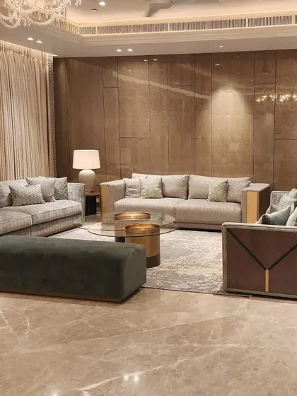 A real-life view of the Sekhri family residence at DLF Camellias. The design focuses on a warm, inviting atmosphere with plush grey sofas, a deep green ottoman, and layered textures that create a sense of quiet luxury.