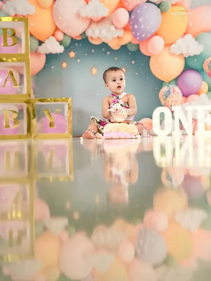 A sweet first birthday cake smash. This little girl is surrounded by a beautiful pastel balloon arch, creating a dreamy and festive scene.