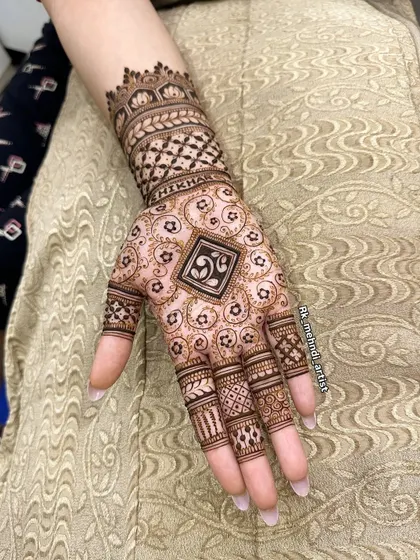 An intricate design featuring a central geometric shape with the initial 'S' inside. The surrounding patterns are delicate and beautiful.