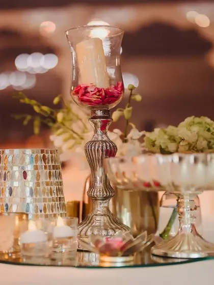 A close-up of a table centerpiece from the royal-themed engagement. The design includes delicate florals, candles, and metallic vases on a mirrored base to reflect the ambient light beautifully.
