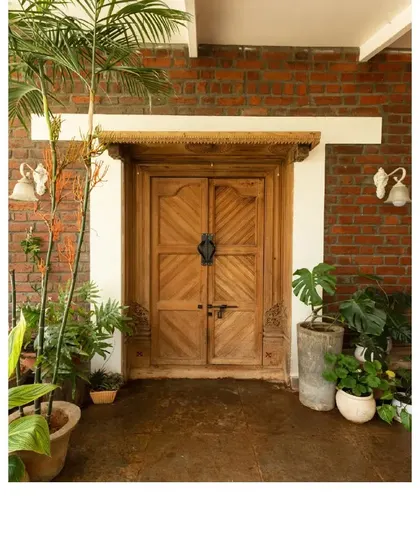 The main entrance to The Brick Loft, featuring a beautifully crafted repurposed wooden door against a backdrop of exposed brick and lush plants.