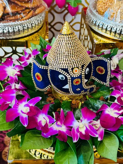 A stunningly decorated coconut featuring a Ganesha motif made from blue velvet and studded with stones. It is surrounded by fresh orchids, making it a luxurious centerpiece.