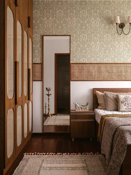 This guest bedroom is all about quiet comfort. We used mellow floral wallpaper, cane accents on the headboard and wardrobe, and touches of brass to create a warm, familiar, and welcoming space.