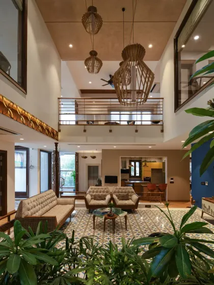 The Ashraya Residence is organized around a central, double-height courtyard that connects all spaces. This view from the indoor greenery looks up towards the first-floor lounge, showcasing the home's vertical connectivity and Indian-inspired theme.