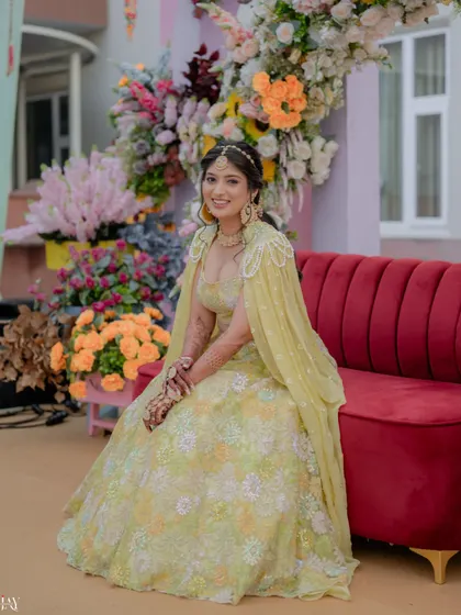 The bride seated on a red sofa, looking radiant and happy amidst the colorful Haldi decor.