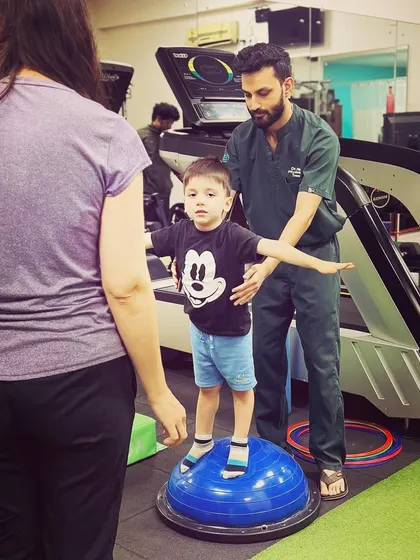 Our care extends to the youngest members of your family. Here, one of our expert physiotherapists guides a child through a balance and coordination exercise on a BOSU ball, making pediatric therapy engaging and effective.