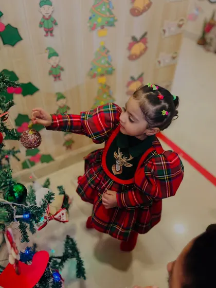 A beautifully dressed toddler hangs an ornament, fully engaged in the magic of decorating the Christmas tree.