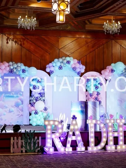 We create immersive underwater worlds with our mermaid-themed stage setups. This design for 'RADHIA' features pastel balloon arches, coral-like structures, and backdrops depicting a magical ocean scene, complete with marquee letters.