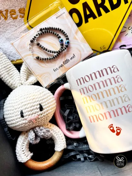 A thoughtful hamper for the mom and baby, featuring a 'Momma' mug, a crochet bunny rattle, and a delicate 'nazariya' bracelet for the little one.