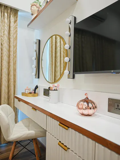 The vanity area in the master bedroom features a sleek white dresser with fluted details, a round mirror, and classic makeup lights for a touch of Hollywood glamour.