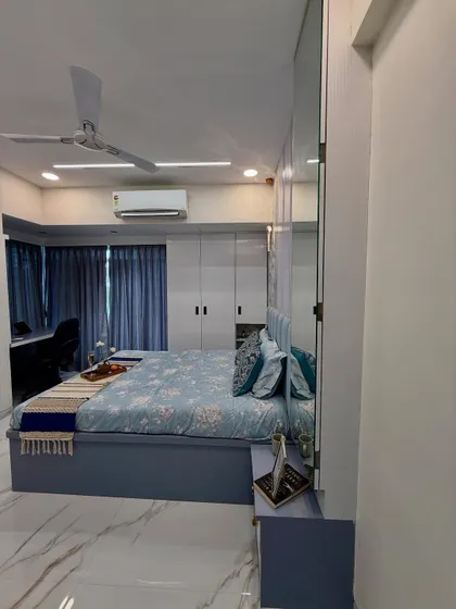 A full view of a master bedroom with a cool blue color scheme, floor-to-ceiling wardrobes, and an integrated study or dressing table. The mirrored wardrobe panels make the room feel larger.