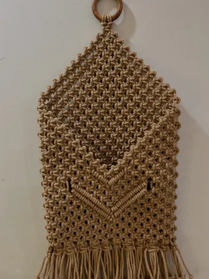 A full, straight-on view of the macrame pocket organizer. The V-shaped detail on the pocket adds a lovely design element.