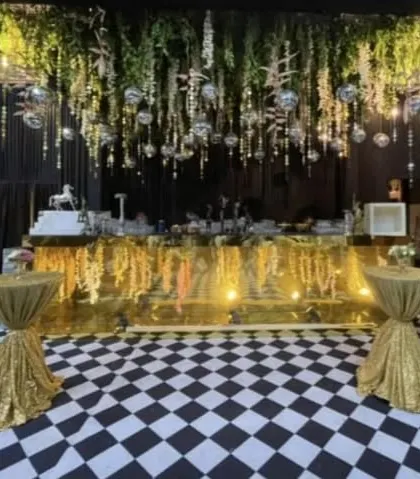 A unique bar and lounge area with a checkered floor. The gold bar, hanging greenery, and disco balls create a fun and glamorous vibe for a cocktail party.