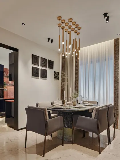 The dining area features a striking chandelier with cascading wooden elements over a dark marble table. This space is designed for both formal entertaining and comfortable family meals, flowing seamlessly from the living room.