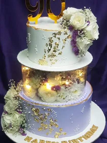This two-tier floral cake is designed with a lighted separator, creating a beautiful glow from within. Adorned with white roses and gold leaf, it's a stunning choice for a 90th birthday.