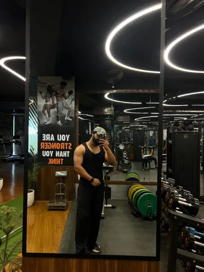 A full view of our gym floor in the mirror. This shot showcases the clean, organized space, with weight plates stacked, cardio machines in the background, and motivational posters on the wall.