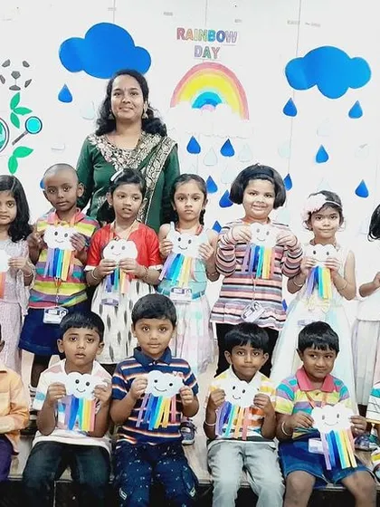 A class poses with their teacher, all holding their rainbow crafts, capturing a moment of collective achievement.