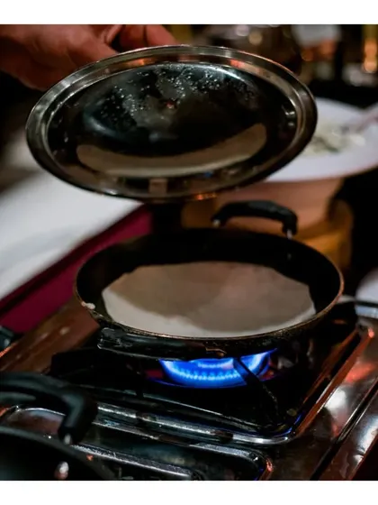 A chef preparing a fresh appam, a popular South Indian rice pancake, at a live station.