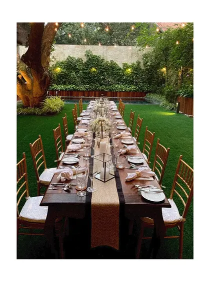 A beautifully set long table in an outdoor garden, ready for a daytime event. The simple elegance of the setup allows the natural surroundings to shine.