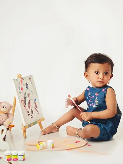 A curious glance from the artist at work. The clean white background makes the colors of the paint and the baby's outfit stand out.